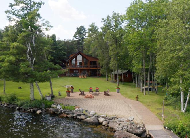 View from the lake showing docking, beach, patio fireplace, grassy yard, and large two level Red Pine Retreat.